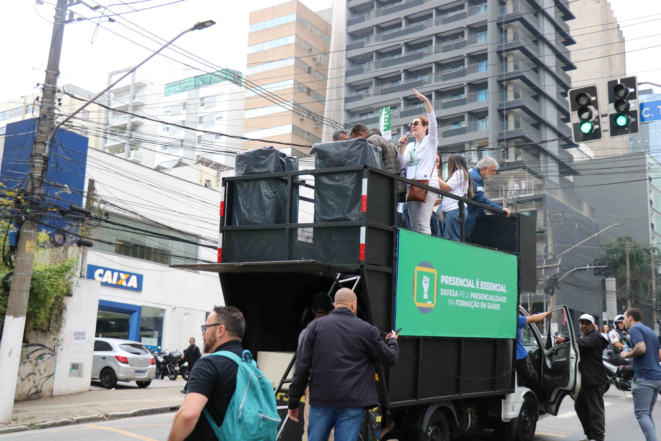 Carro de som preto à frente dos manifestantes na Avenida Brigadeiro Luís Antônio. Em cima do carro de som, a presidente do Fcafs-SP, Juliana Mendes.