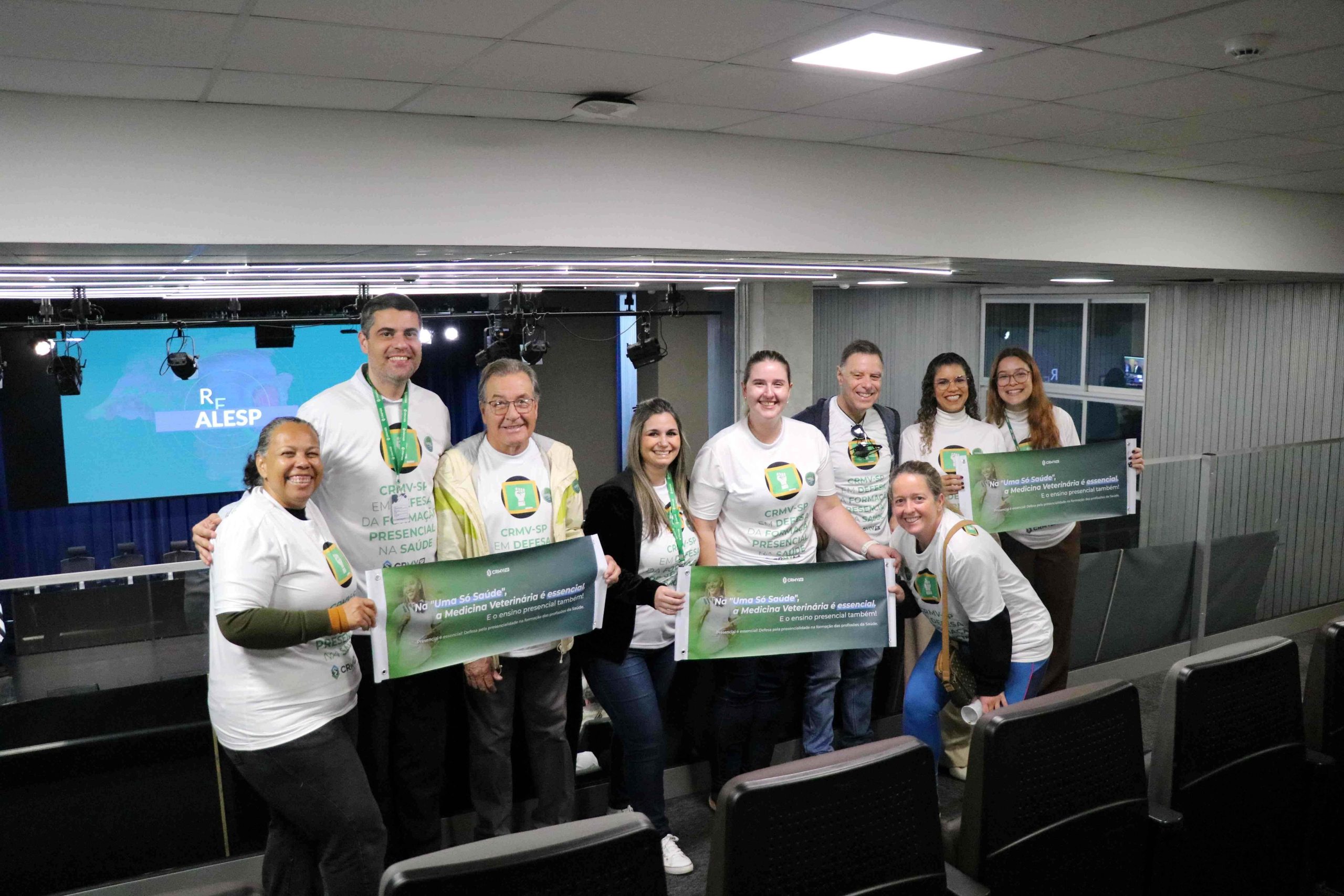 Pessoas em pé, homens e mulheres, vestindo blusa branca pousando para foto.