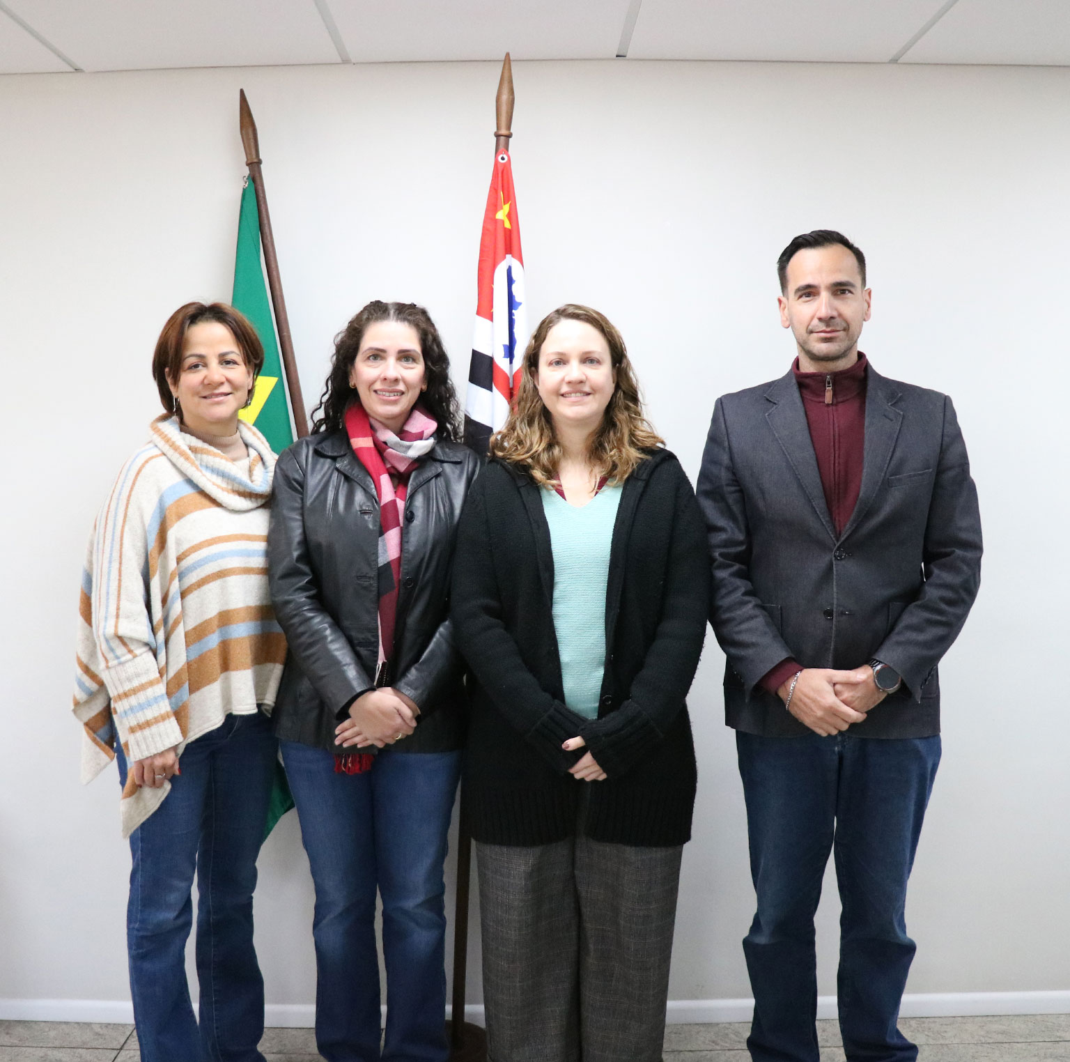 Quatro pessoas em pé pousando para foto na frente de duas bandeiras: uma do Brasil e outra do estado de São Paulo. As pessoas são da esquerda para a direita: a tesoureira Alessandra Marnie, a vice-presidente Carolina Saraiva de Filippos, a presidente Daniela Pontes Chiebao e o secretário-geral, Rodrigo Mainardi.