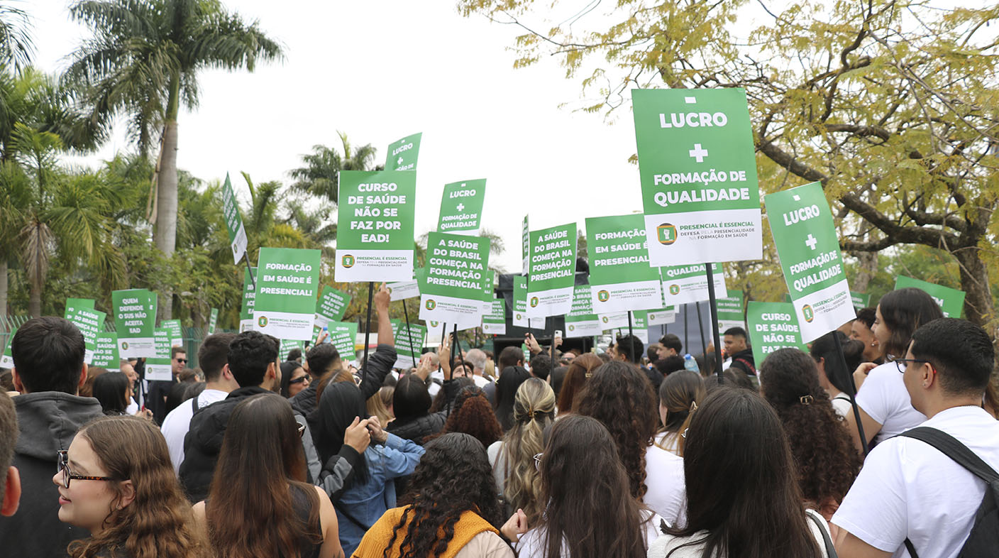 Pessoas mobilizadas em caminhada pelas ruas da cidade, empunhando cartazes em defesa da graduação 100% presencial.