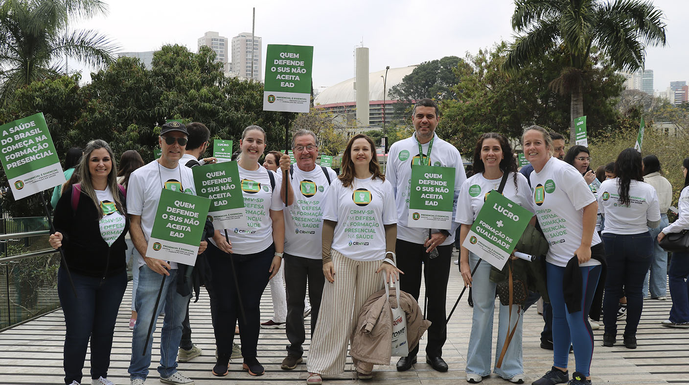 Oito pessoas, cinco mulheres e três homens, durante mobilização em defesa da graduação 100% presencial, empunhando cartazes, em frente à Alesp, em São Paulo.