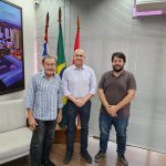 Na foto, estão três homens posando para a foto dentro do gabinete do vice-prefeito de Presidente Prudente. Ao fundo três bandeiras: Brasil, estado de São Paulo e município de Presidente Prudente.