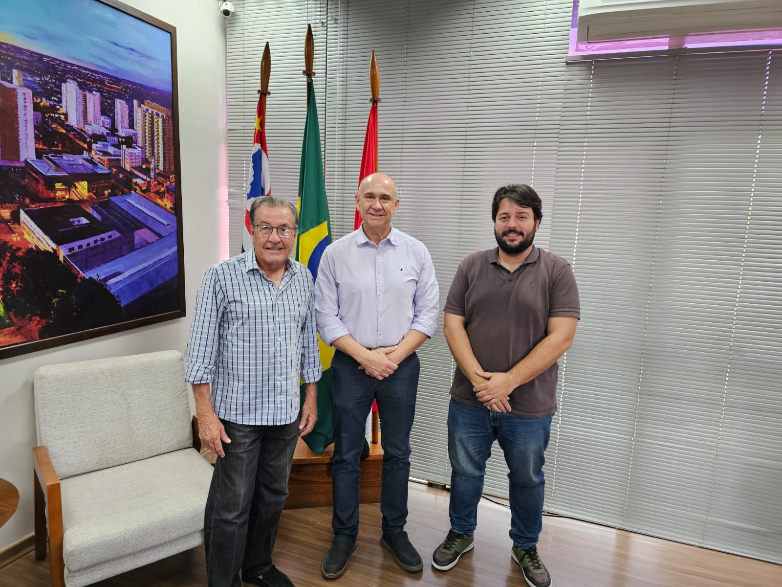 Na foto, estão três homens posando para a foto dentro do gabinete do vice-prefeito de Presidente Prudente. Ao fundo três bandeiras: Brasil, estado de São Paulo e município de Presidente Prudente.