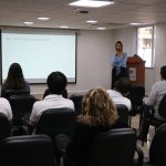 Funcionários do CRMV-SP sentados no auditório enquanto mulher branca de fios loiros lisos médios, vestindo blusa azul clara e calça preta social, fala no microfone. É a dra. Ingrid Bueno Atayde Machado.
