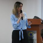Mulher loira de fios lisos na altura do busto, ela veste blusa azul clara com botões no meio e calça social preta, falando no microfone. É a presidente da Comissão de Atenção à Saúde Mental dos Médicos-veterinários e Zootecnistas, Ingrid Bueno Atayde Machado.