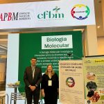 Homem e mulher posando para foto em fachada de evento.