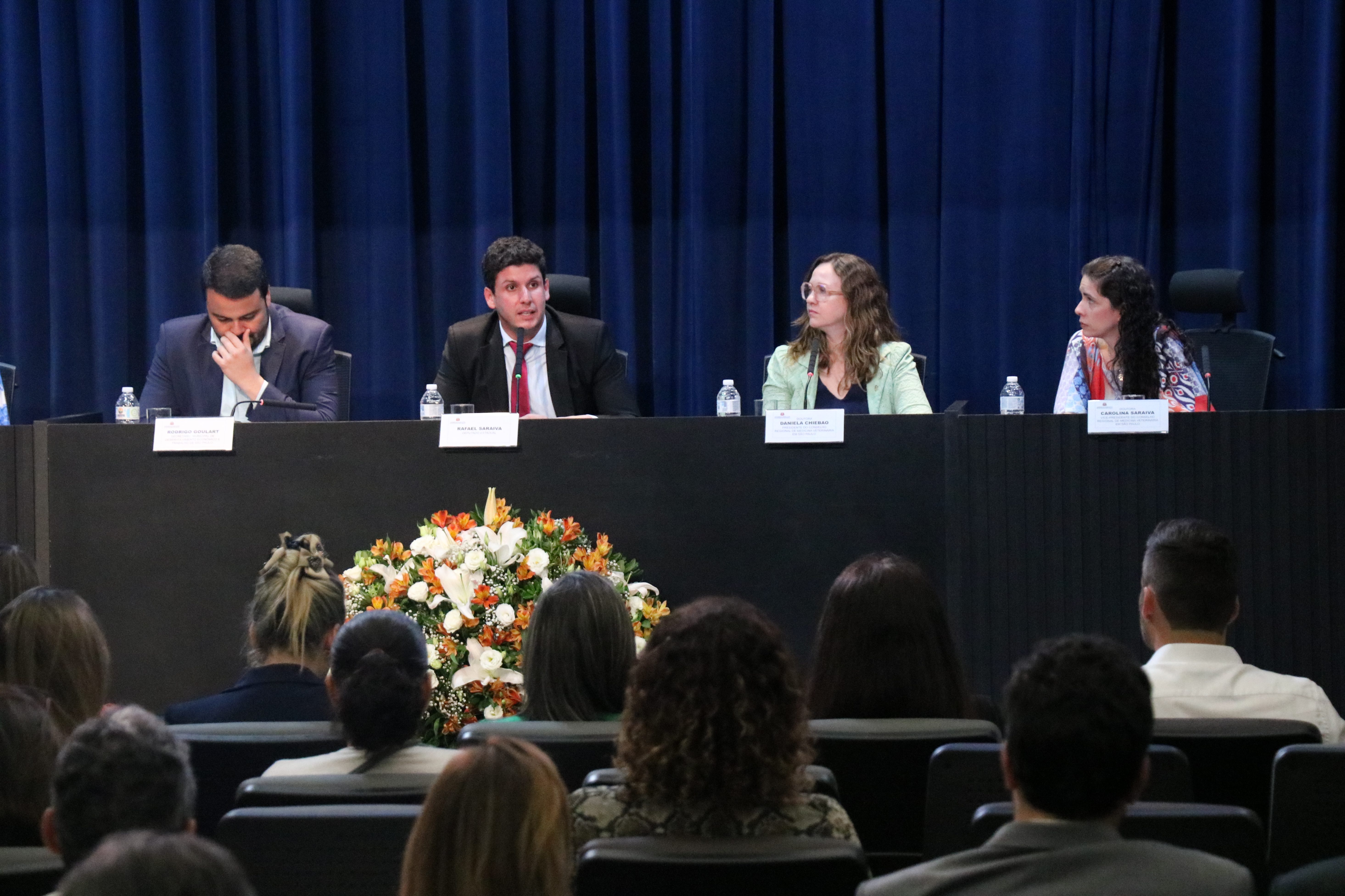 Quatro autoridades reunidas em auditório oficial, todas sentadas. Da esquerda para a direita: o secretário de Desenvolvimento Econômico e Trabalho da Prefeitura de São Paulo e médico-veterinário, Rodrigo Goulart, o deputado estadual Rafael Saraiva, a presidente do CRMV-SP, Daniela Pontes Chiebao e a vice presidente do CRMV-SP, Carolina Filippos.