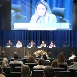 Autoridades sentadas no palco em auditório oficial na Alesp. Da esquerda para a direita: Em pé no púlpito, a coordenadora técnica médica-veterinária do CRMV-SP, Carla Maria Figueiredo de Carvalho e sentados: o secretário-geral do CRMV-SP, Rodrigo Mainardi, a presidente da Comissão de Atenção à Saúde Mental dos Médicos-veterinários e Zootecnistas do CFMV, Ingrid Machado, o secretário de Desenvolvimento Econômico e Trabalho da Prefeitura de São Paulo, Rodrigo Goulart, a presidente do CRMV-SP, Daniela Pontes Chiebao e a vice-presidente do CRMV-SP, Carolina Filippos.