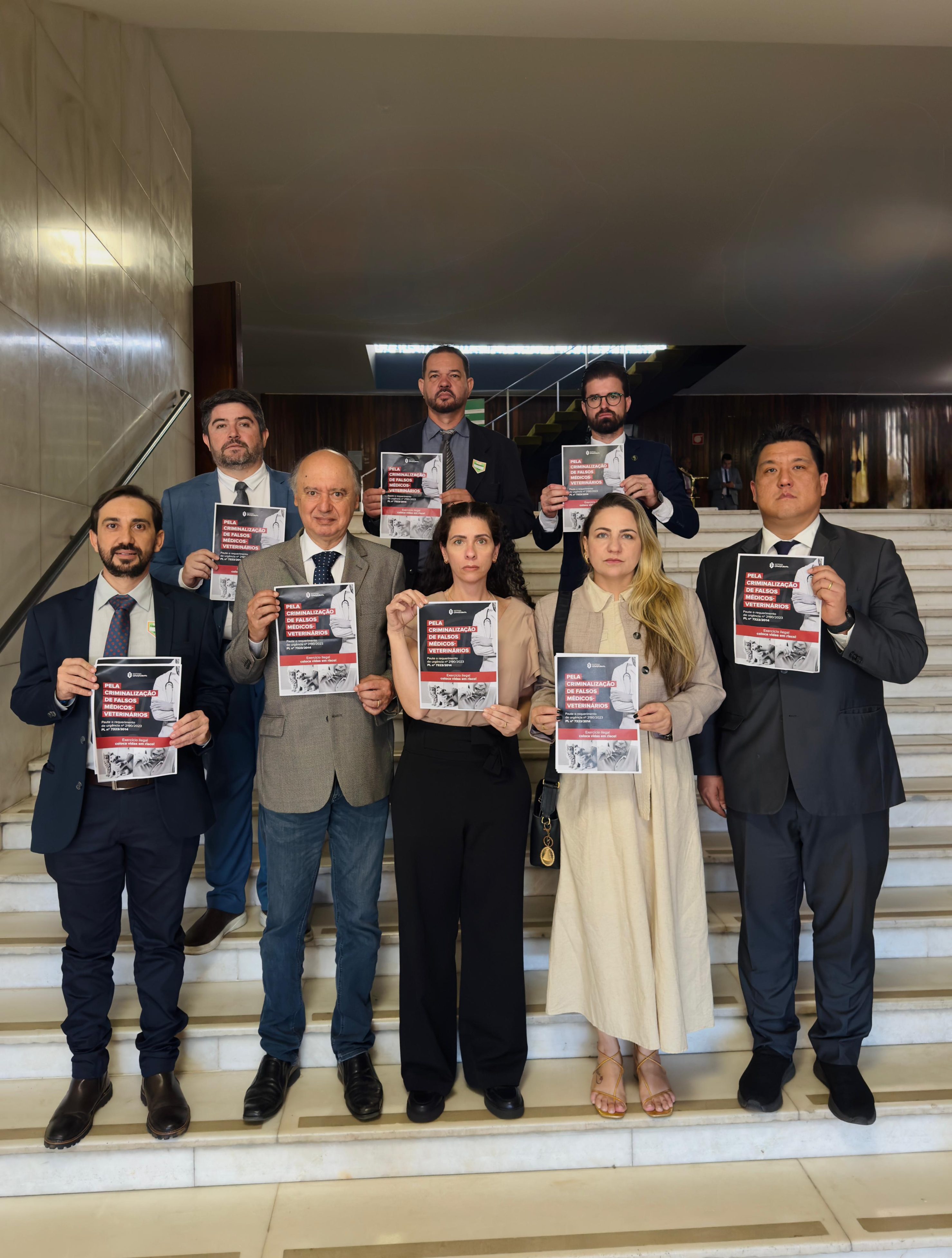 Oito pessoas, duas mulheres e seis homens, reunidas em escadaria segurando papel para foto.