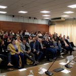 Pessoas sentadas assistindo a uma pessoa falando ao microfone.