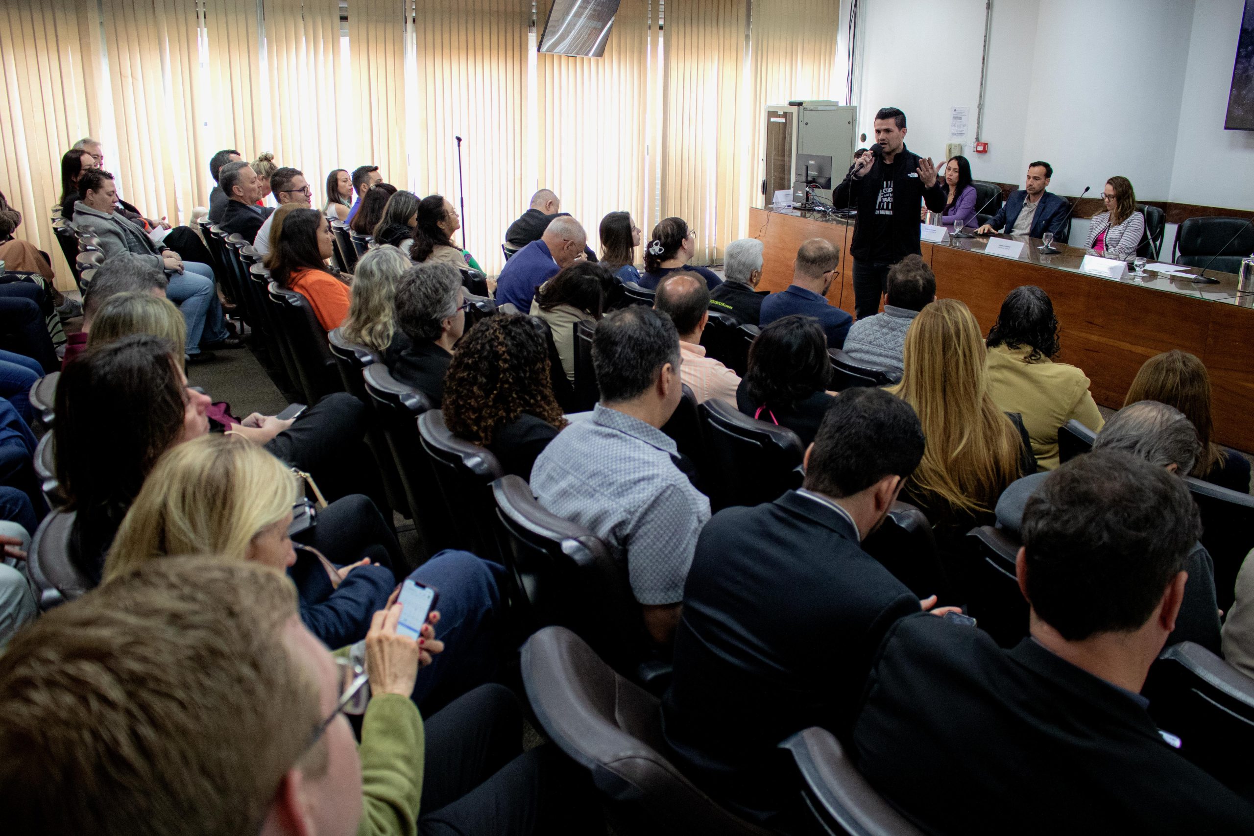 Pessoas sentadas assistindo a uma pessoa falando ao microfone.