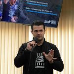 Homem branco de olhos pretos e cabelo preto liso curto vestindo blusa de algodão preta com a estampa em letras brancas: "Cadeia para Maus Tratos, Dr. Murillo Lima." e casaco preto, falando no microfone. É o vereador e médico-veterinário por São Paulo, Murillo Lima.