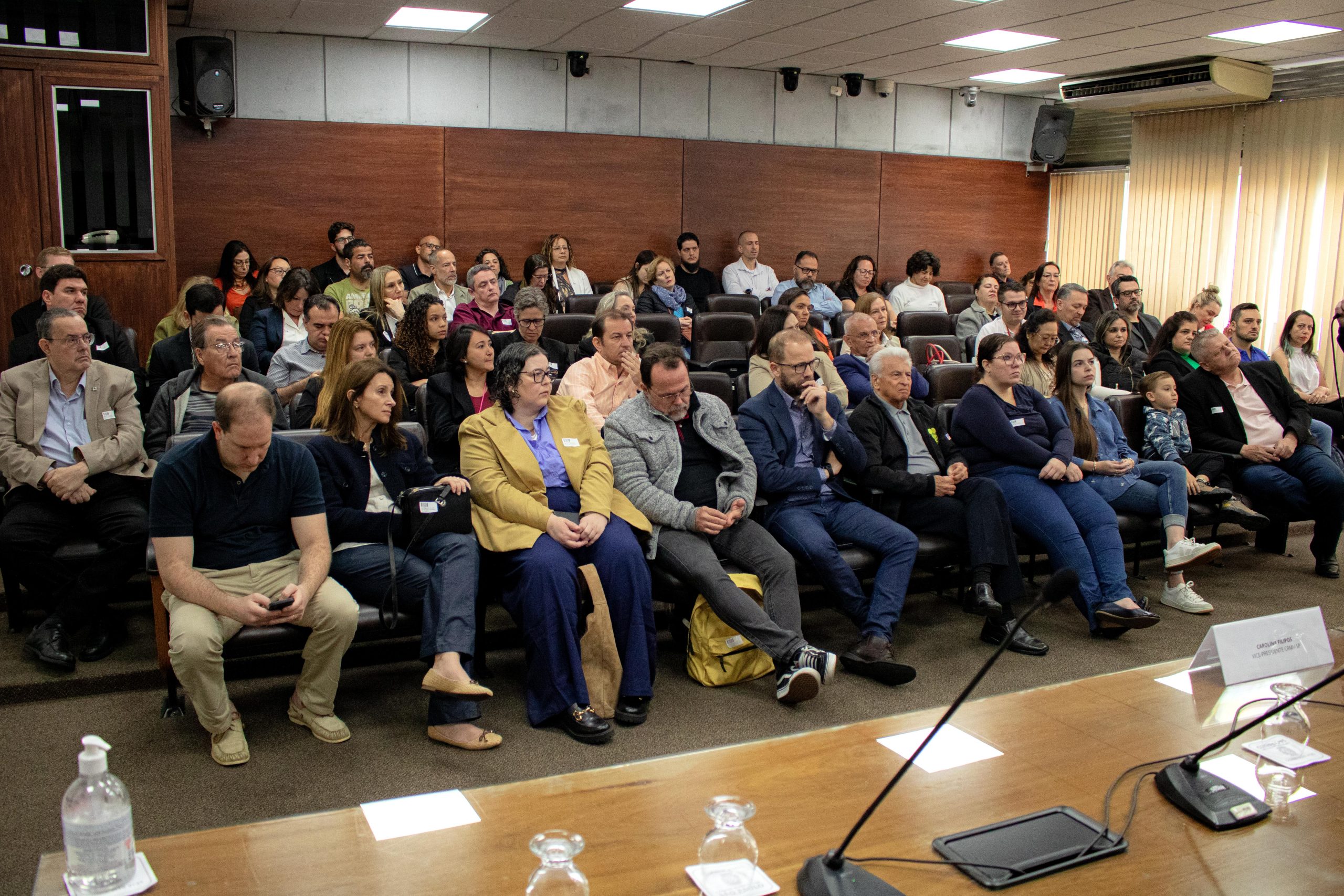 Pessoas sentadas em uma sala na Câmara Municipal observando uma palestra.
