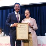 Homem e mulher em palco posando para foto segurando placa de homenagem. A mulher é a presidente do CRMV-SP, Daniela Pontes Chiebao.