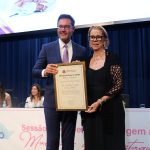 Homem e mulher em palco posando para foto segurando diploma de homenagem. A mulher é a presidente do CFMV, Ana Elisa Fernandes de Souza Almeida.