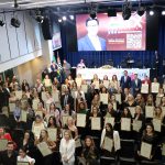 Pessoas reunidas em auditório na Alesp posando para foto segurando diplomas.