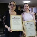 Duas mulheres posando para foto segurando placa de homenagem.