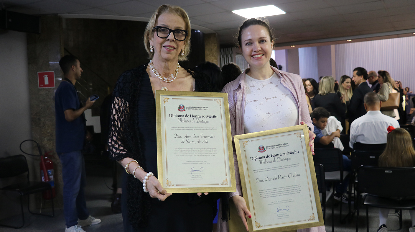 Duas mulheres posando para foto segurando placa de homenagem.