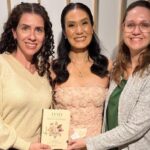Mulheres reunidas para foto com livro.