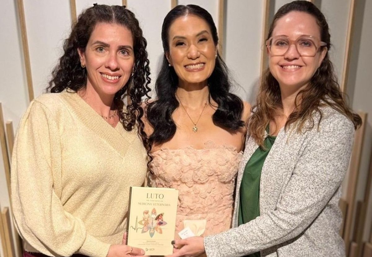 Mulheres reunidas para foto com livro.