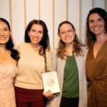 4 mulheres reunidas com livro posando para foto.