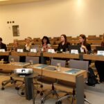 Pessoas sentadas a mesa, assistindo a palestra.