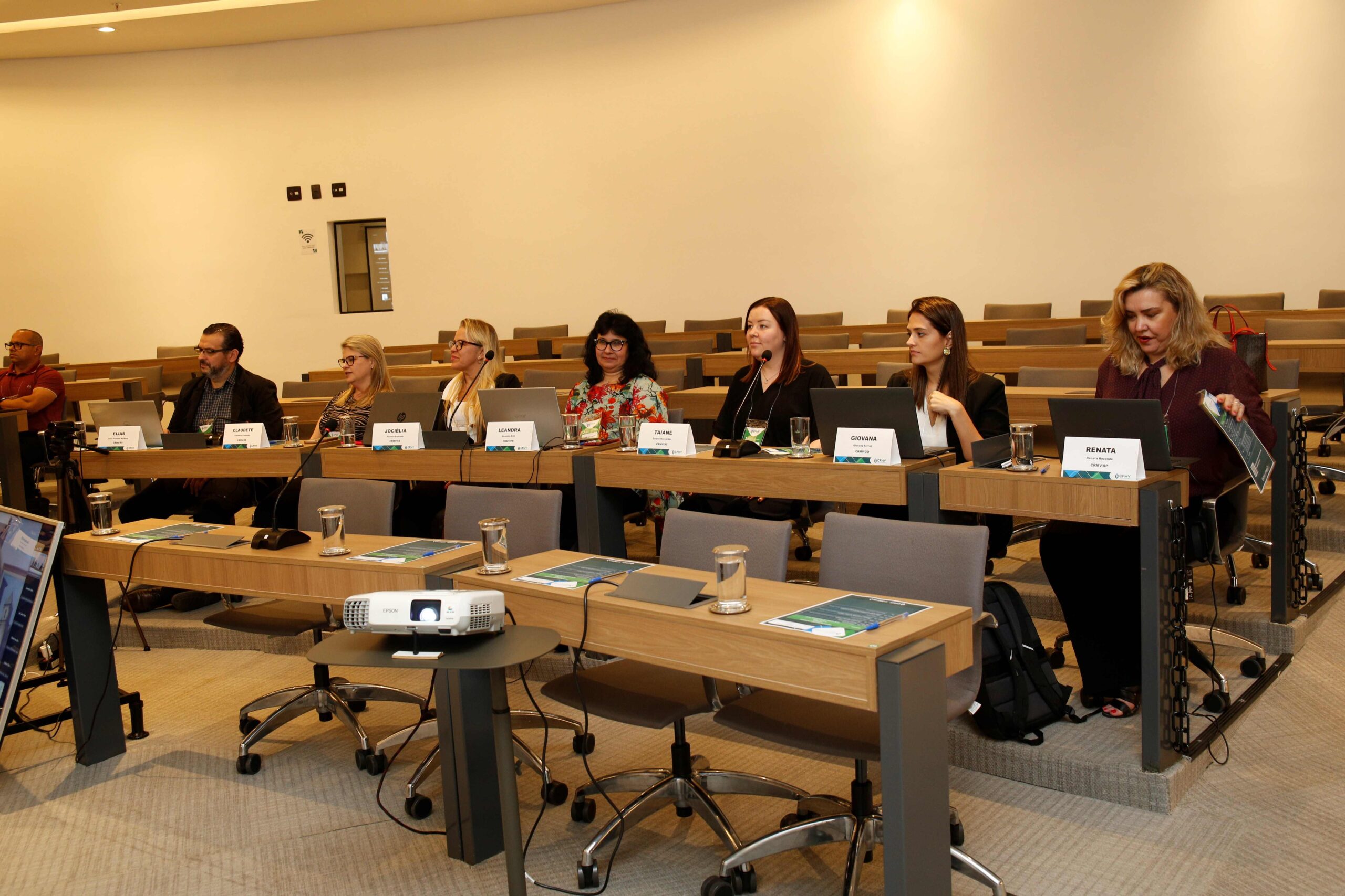 Pessoas sentadas a mesa, assistindo a palestra.