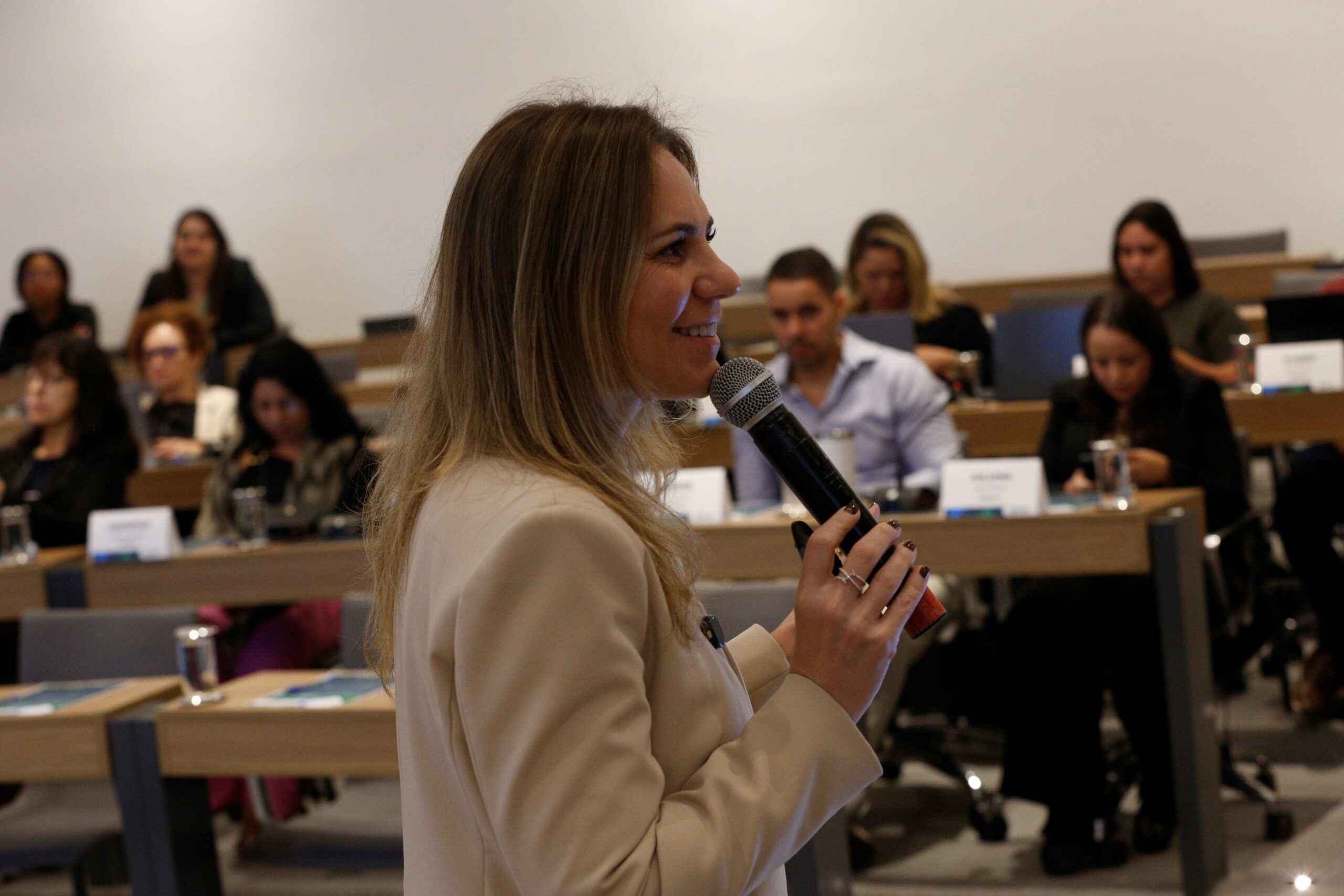 Mulher falando no microfone frente ao público.