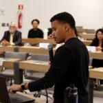 Homem falando no microfone frente ao público.