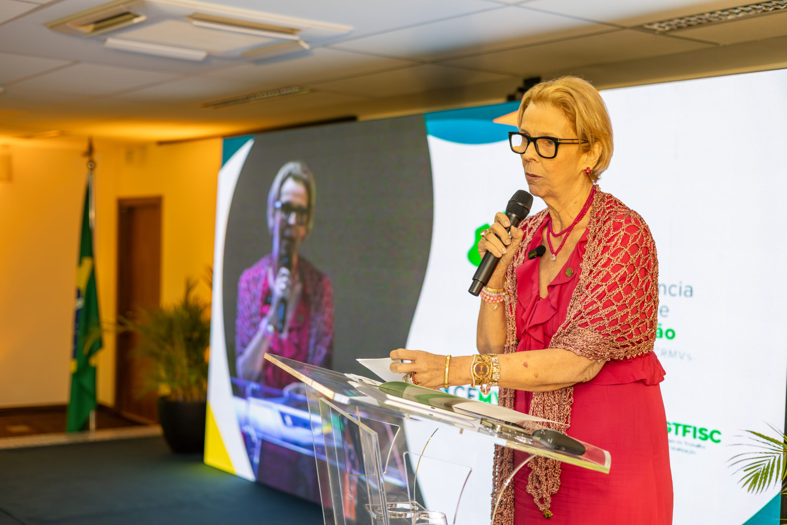 Mulher falando no microfone em palco.