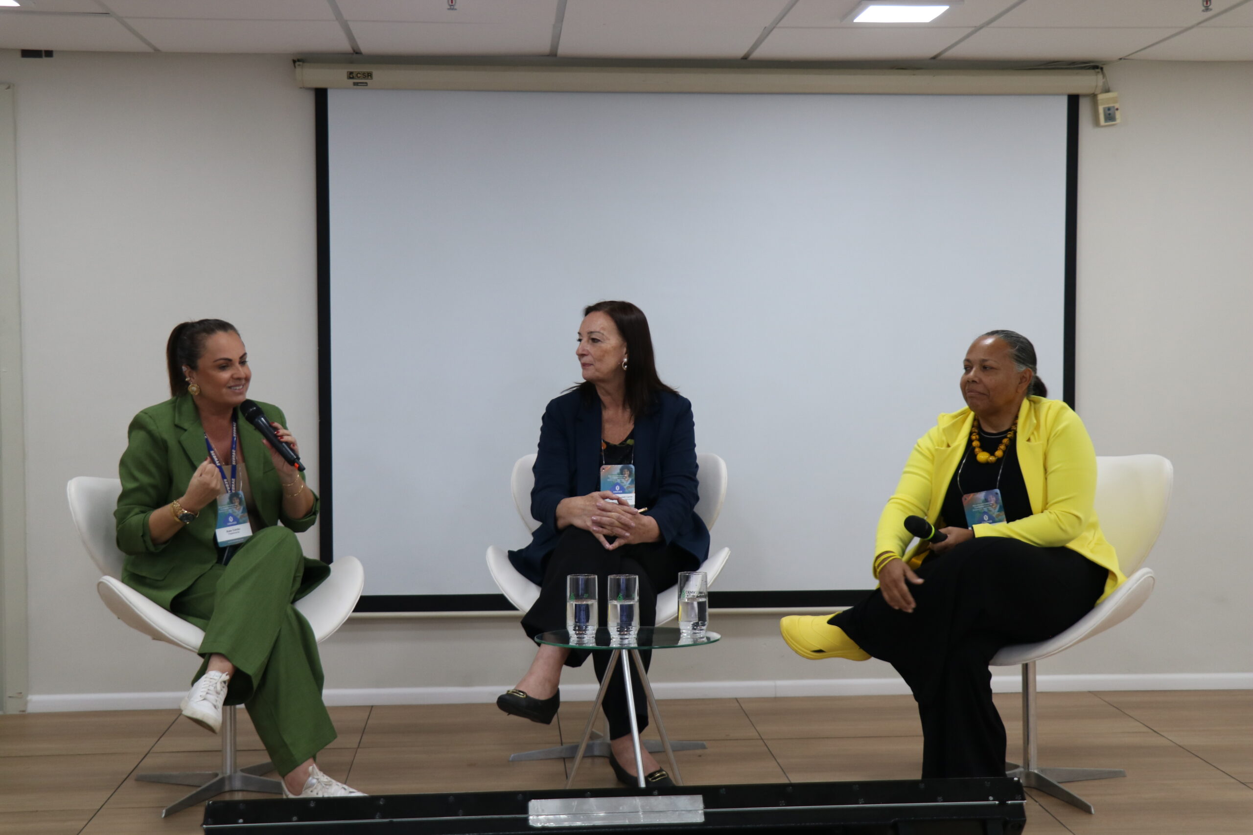 3 mulheres em uma mesa de discussão num auditório