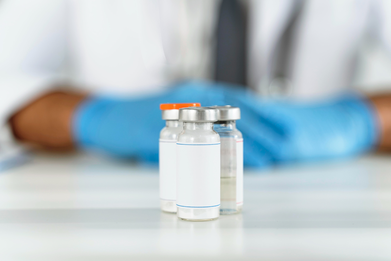 3 Frascos de remédio com uma pessoa ao fundo usando uniforme e luvas brancas.