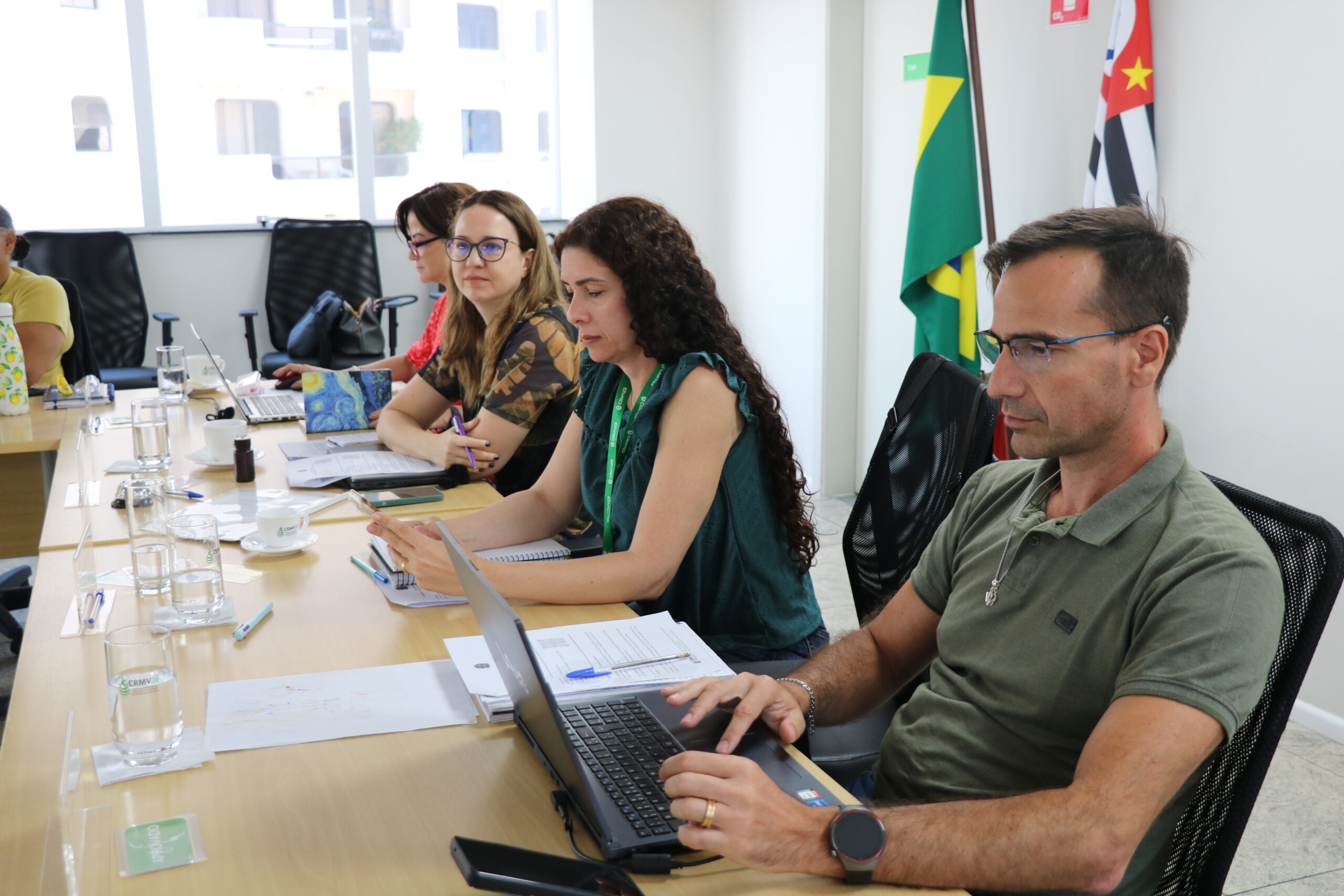 Quatro pessoas à frente em uma sala de reunião, sendo três mulheres e um homem.