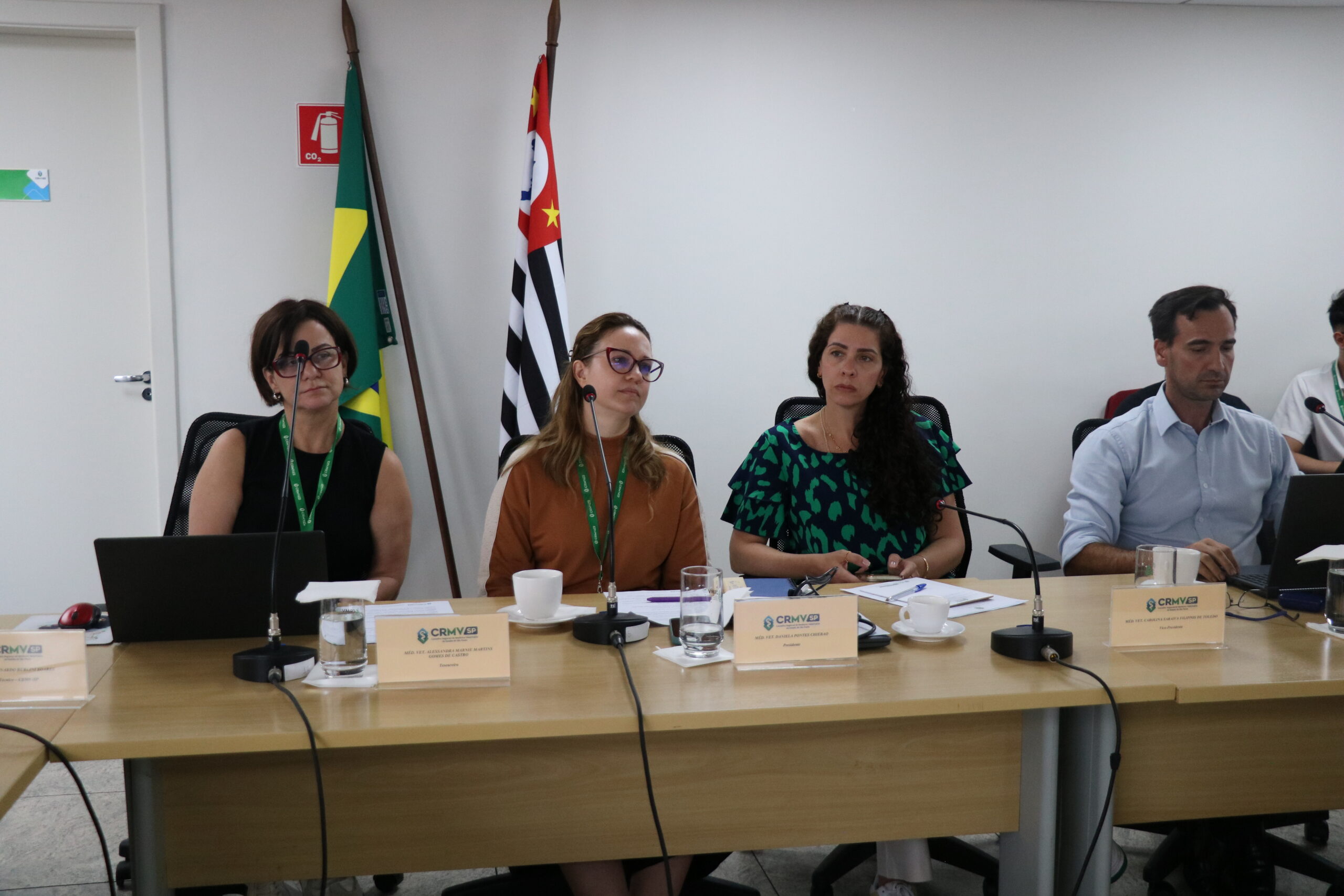 Quatro pessoas à frente em uma sala de reunião, sendo três mulheres e um homem.