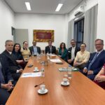 Na imagem há homens e mulheres sentados lado a lado em uma mesa de reunião.