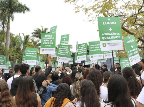 Pessoas mobilizadas em caminhada pelas ruas da cidade, empunhando cartazes em defesa da graduação 100% presencial.