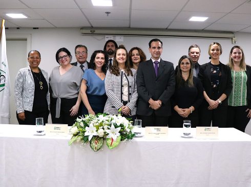 Homens e mulheres em pé pousando, com mesa à frente com arranjo de flores. Esses são os conselheiros e diretores do CRMV-SP para o triênio 2024-2027. Ao centro está a presidente do Regional.