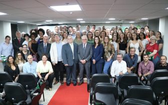 Pessoas, entre mulheres e homens, lado a lado, posam para a foto em auditório, após evento.