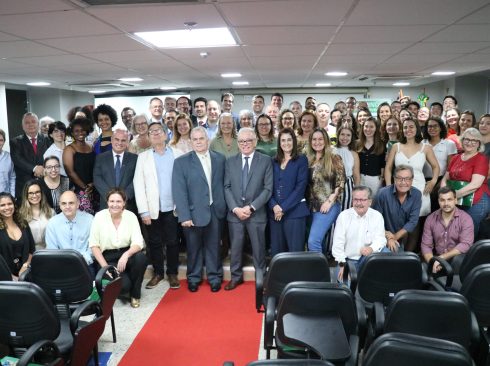 Pessoas, entre mulheres e homens, lado a lado, posam para a foto em auditório, após evento.