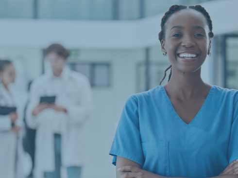 Mulher em pé de braços cruzados usando uniforme azul, sorri para foto.