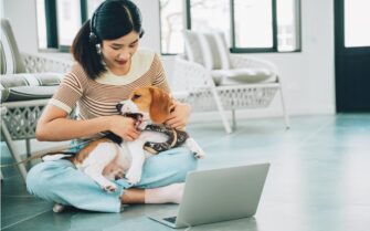 Uma mulher está sentado no chão, com o seu cachorro no colo, em atendimento virtual pelo computador.