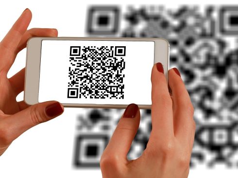 A imagem mostra uma mão que está segurando um celular, registrando um QR Code.
