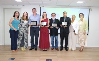 Foto posada da presidente, da vice-presidente, da tesoureira e da presidente da Comissão de Avaliação do CRMV-SP com os quatro premiados de 2025, sendo três homens e duas mulheres. Os premiados estão com as placas nos prêmios em mãos.