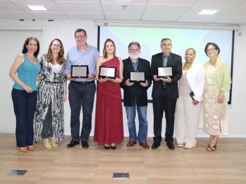 Foto posada da presidente, da vice-presidente, da tesoureira e da presidente da Comissão de Avaliação do CRMV-SP com os quatro premiados de 2025, sendo três homens e duas mulheres. Os premiados estão com as placas nos prêmios em mãos.