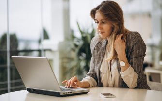 Mulher em uma mesa redonda, fazendo anotações em um notebook.