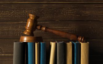 Martelo de madeira marrom utilizado comumente em tribunais deitado sobre livros e processos jurídicos.