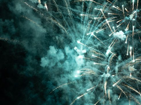Imagem traz uma queima de fogos de artifício branco com fumaça em um céu escuro.