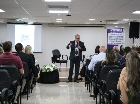 Um homem de terno, se apresenta em auditório para pessoas sentadas em cadeira