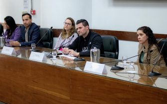Pessoas sentadas apoiando em uma mesa com microfones.