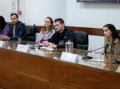 Pessoas sentadas apoiando em uma mesa com microfones.